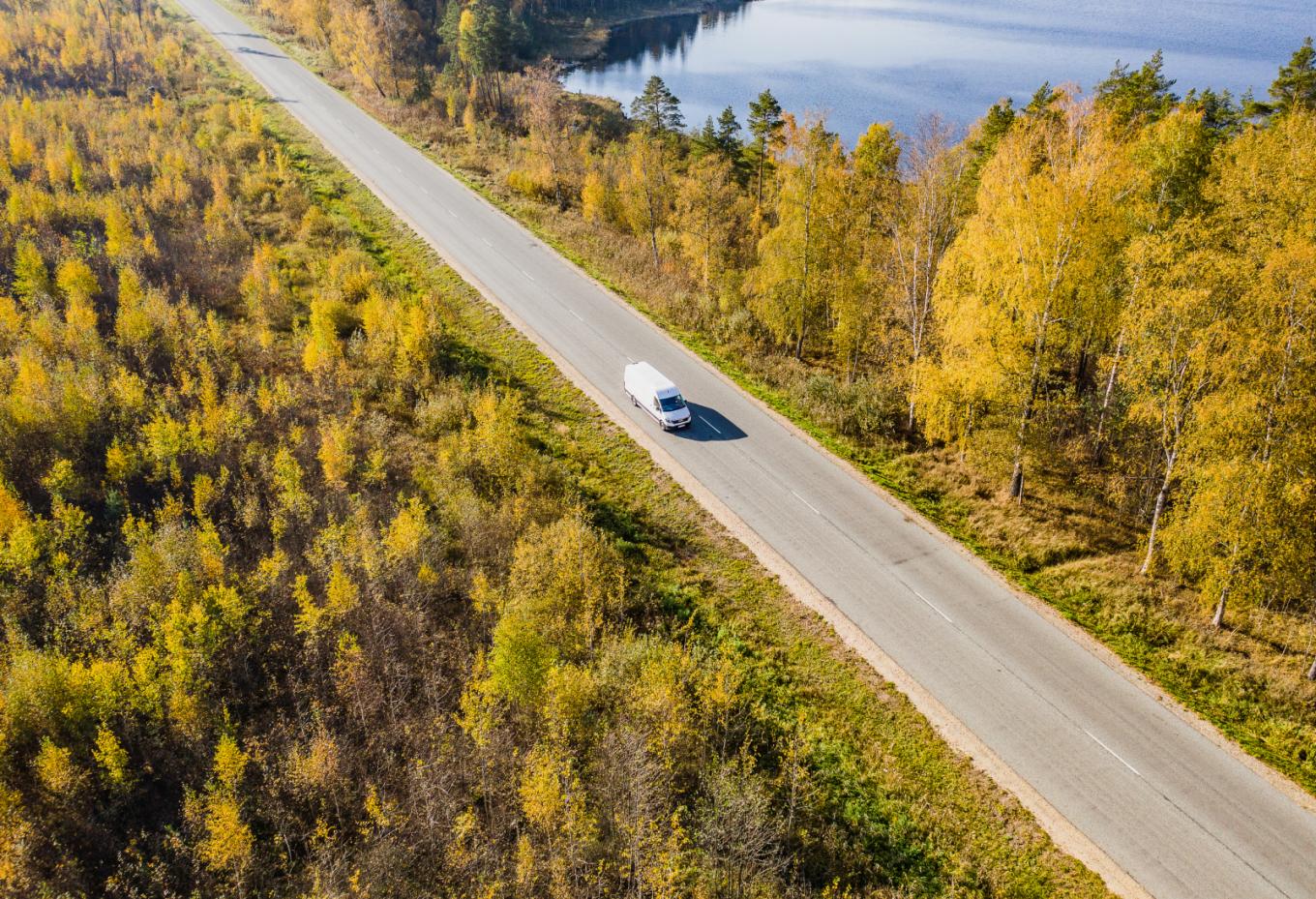 Ein Auto fährt alleine auf einer Landstraße umgeben von Wald