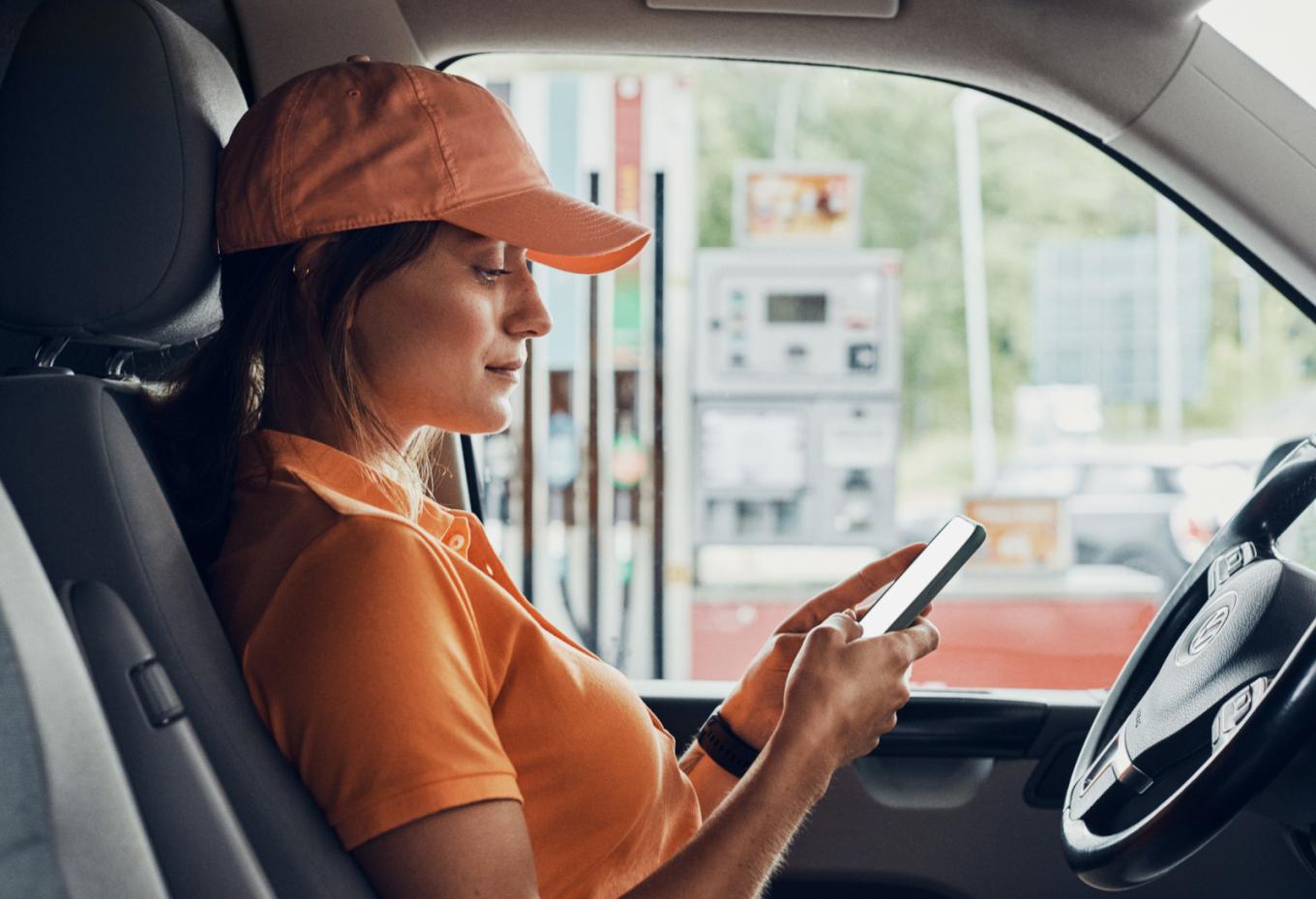 Frau sitzt im Auto und bedient ihr Smartphone